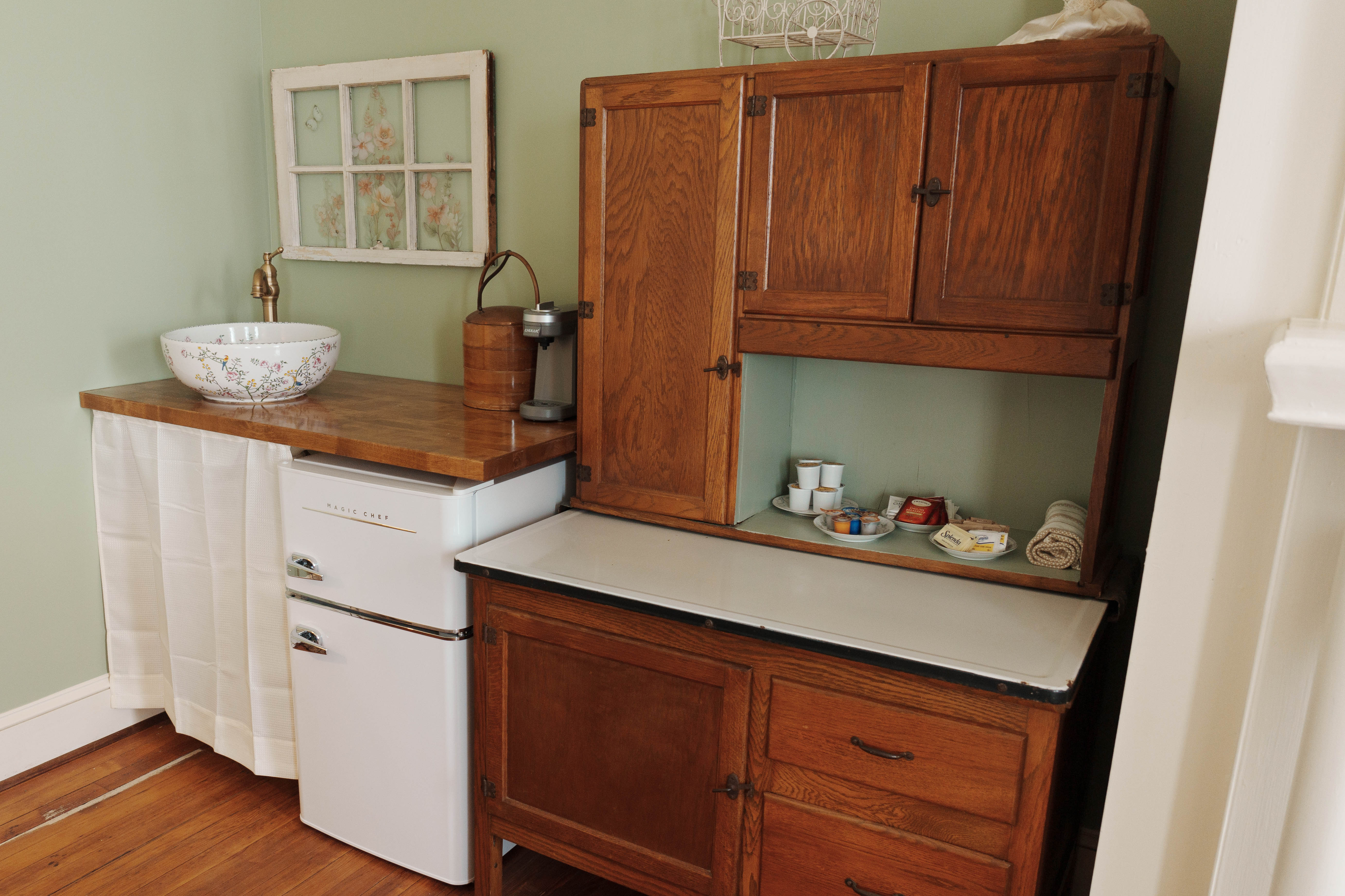 Kitchenette area with oak Hoosier-style hutch, vintage-style mini-fridge, and wooden counter withvessel sink.