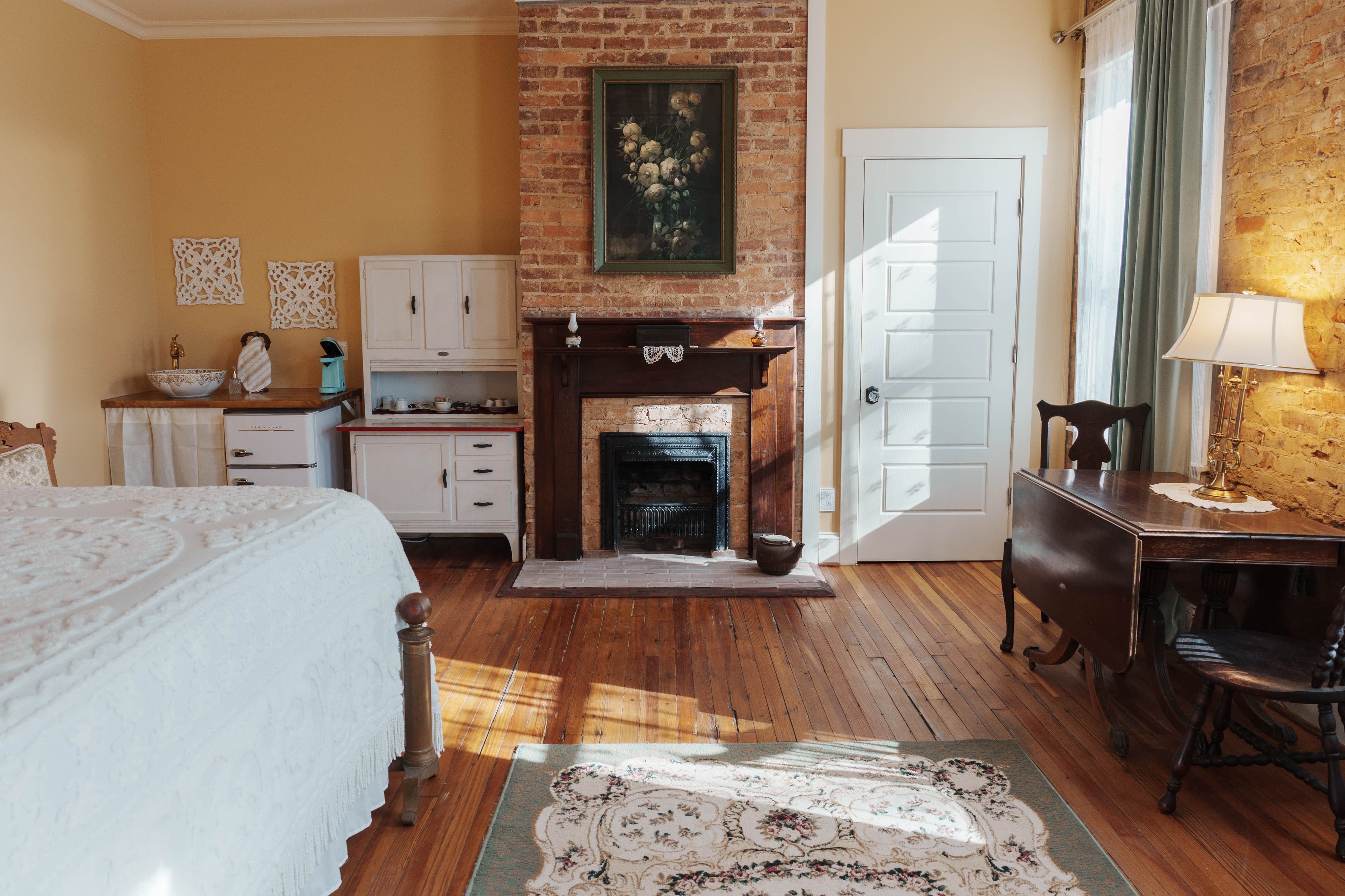 A bedroom with a brick fireplace, a wooden drop-leaf table, and a partially visible bed.