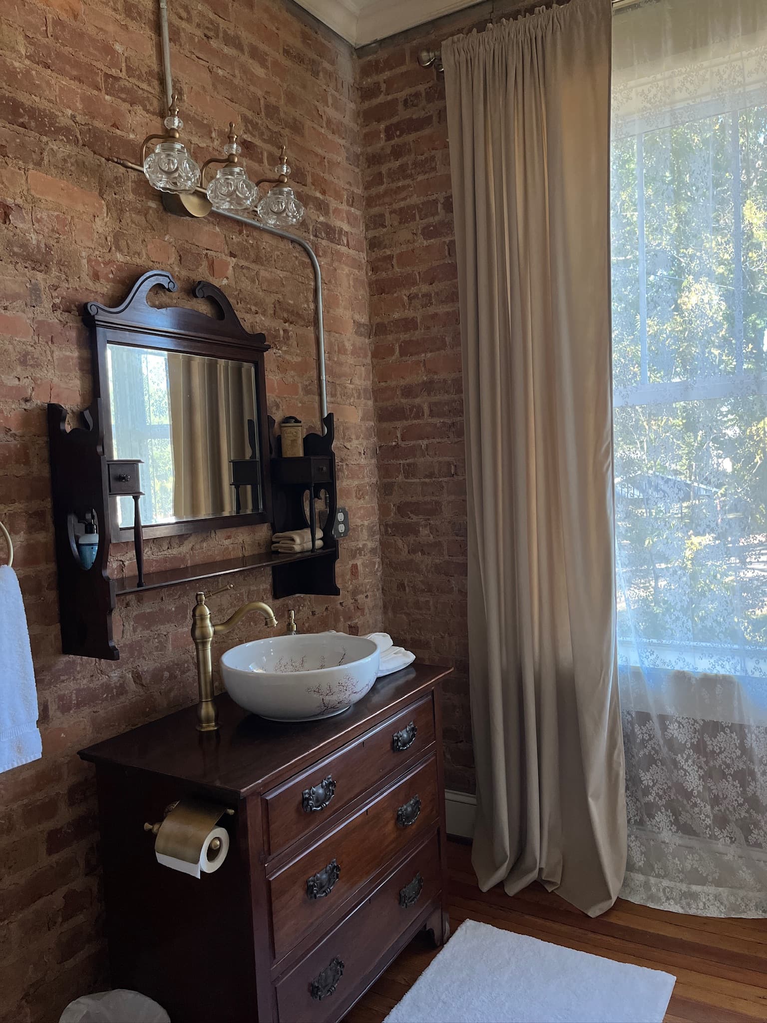 Bathroom dresser-style vanity with bowl sink, mirror, and exposed brick walls.