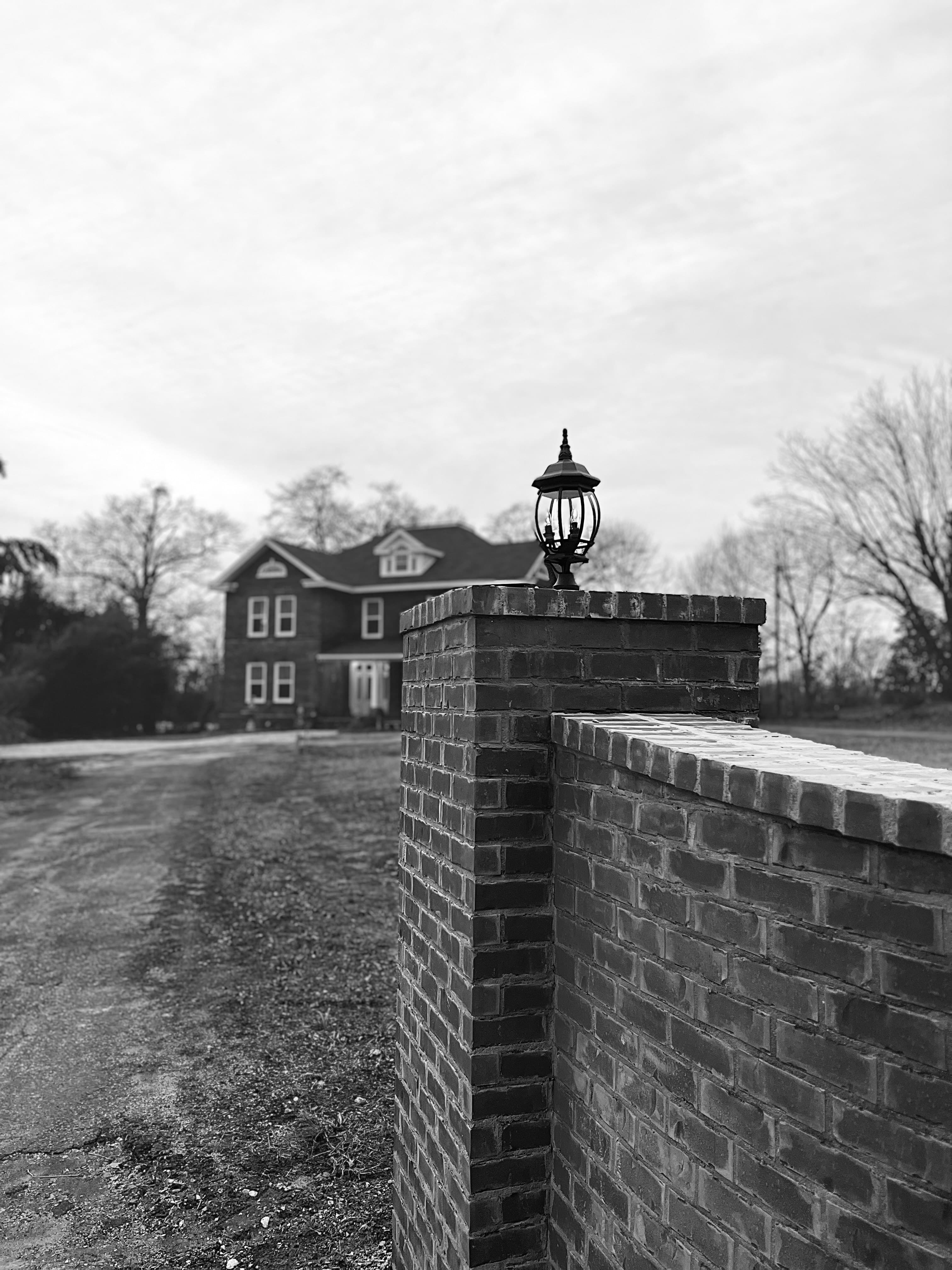 A brick wall with a lantern in the foreground, featuring a house in the background.