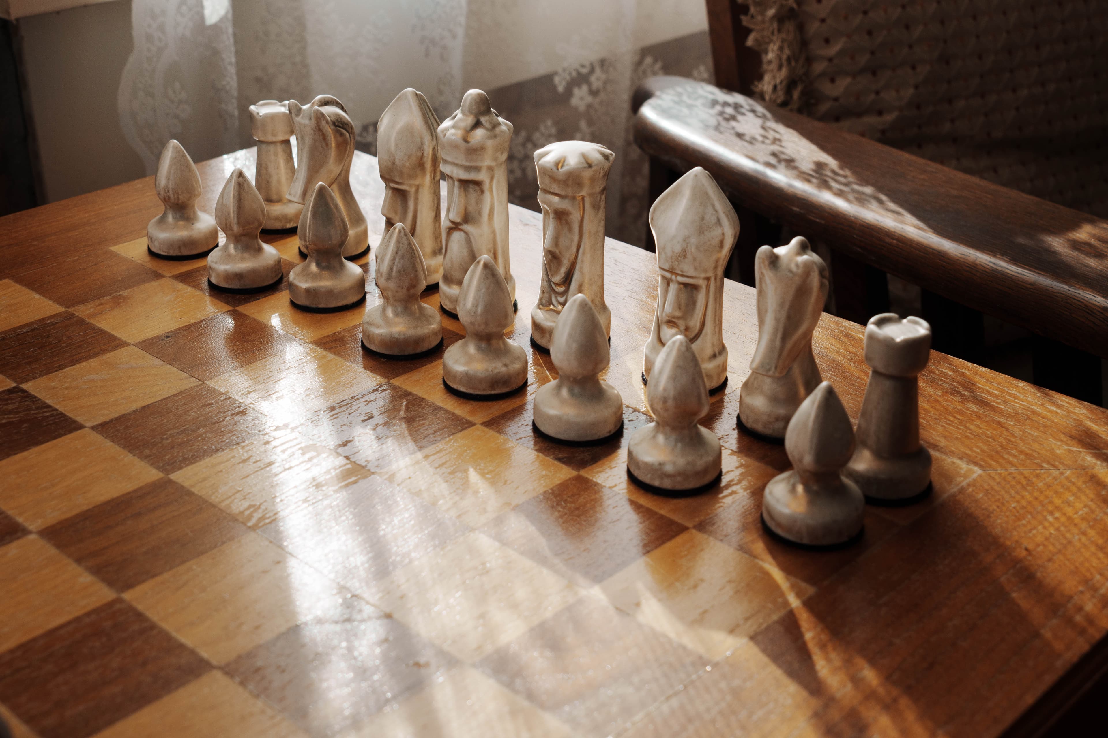 A close-up of a vintage chess set positioned on a wooden board, reflecting sunlight.
