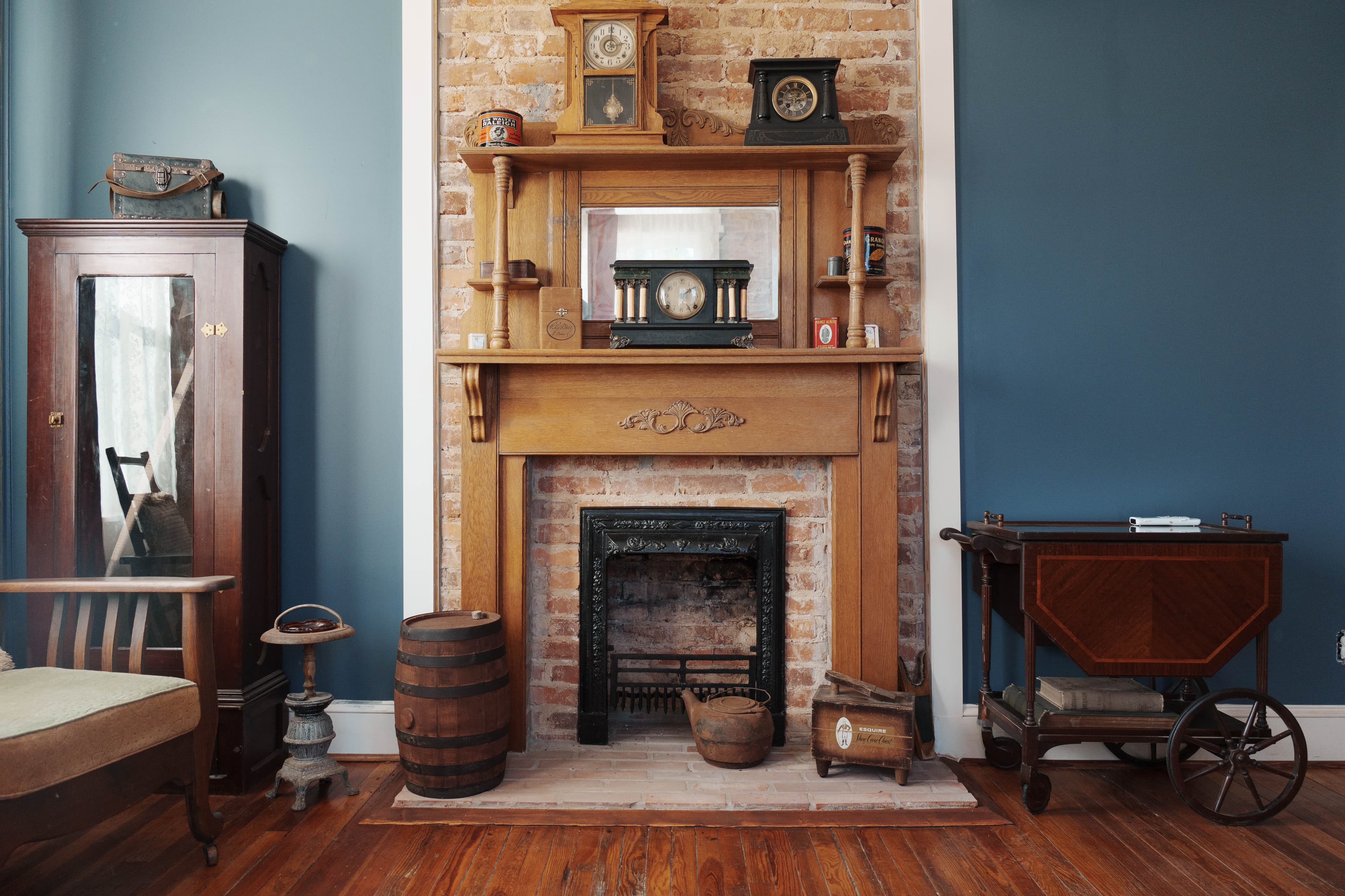 A vintage living room featuring a brick wall fireplace with decorative clocks and antique furnishings.