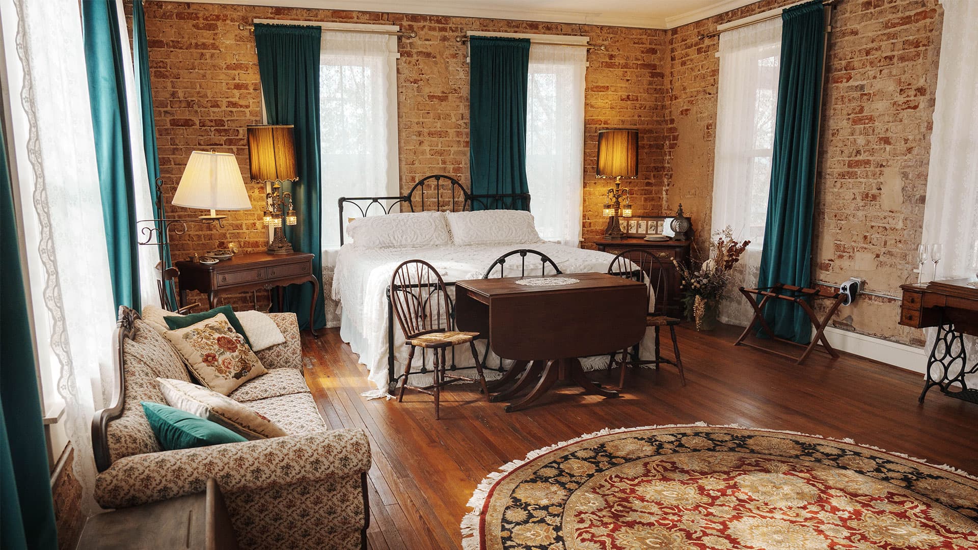 A cozy, warmly lit bedroom featuring a vintage bed, a patterned rug, and rustic brick walls.