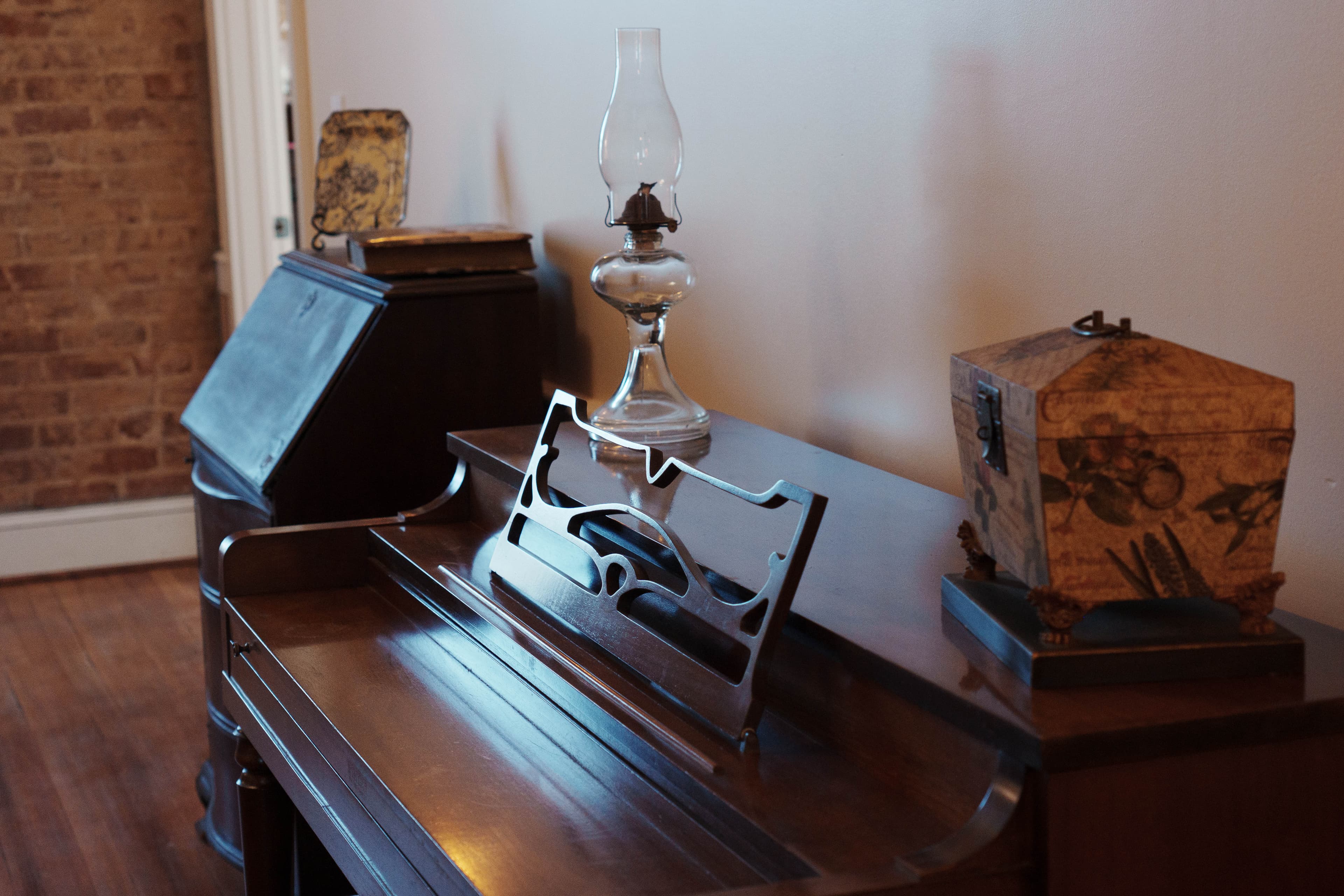 A vintage piano with a music stand, an oil lamp, and a decorative box on a wooden surface.